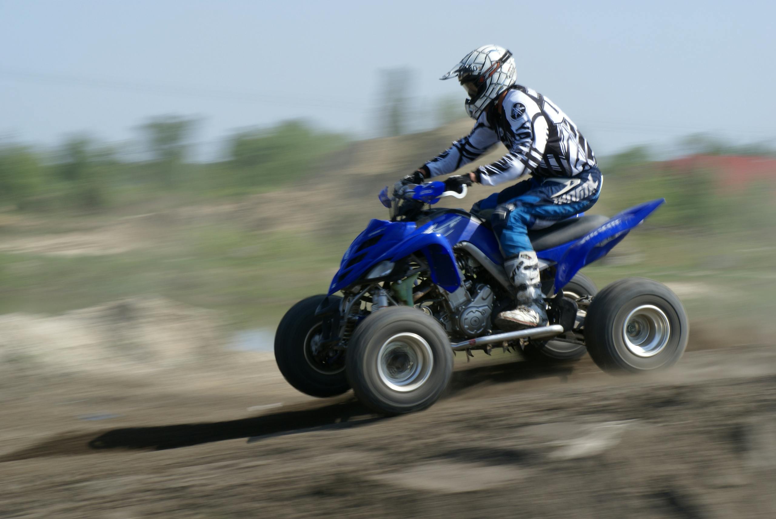 Action-packed image of a rider on a blue ATV speeding across a dirt track.